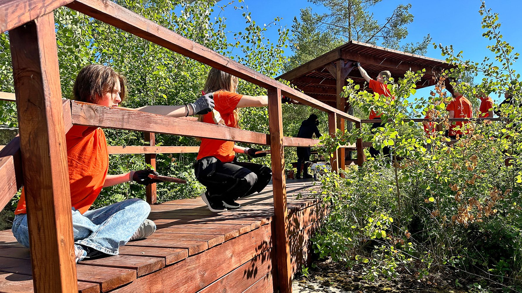 Ungdomar i orange t-shirts oljar in en träkonstruktion.