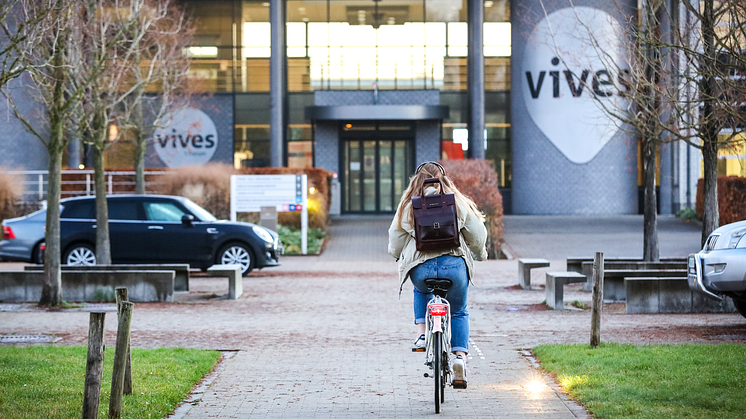 Vives-Hogeschool-Studierende radelt auf Campus mit Vives Logo.png