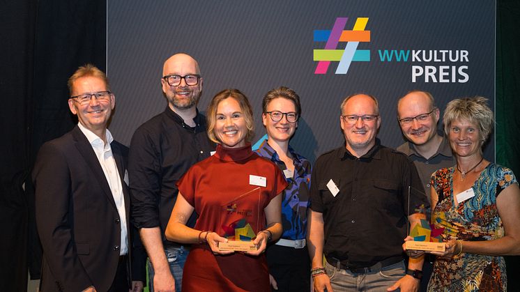 Die Jury-Mitglieder Jürgen Noch (l.) und Dr. In Jana Duda (4.v.l.) gratulieren Kulturamtsleiter Maximilian Zindel,  Julia Ures, Thorsten Hennig, Olaf Menne (alle 0525.1fallsreich) und Sabine Kramm (stellvertretende Bürgermeisterin Stadt Paderborn)​