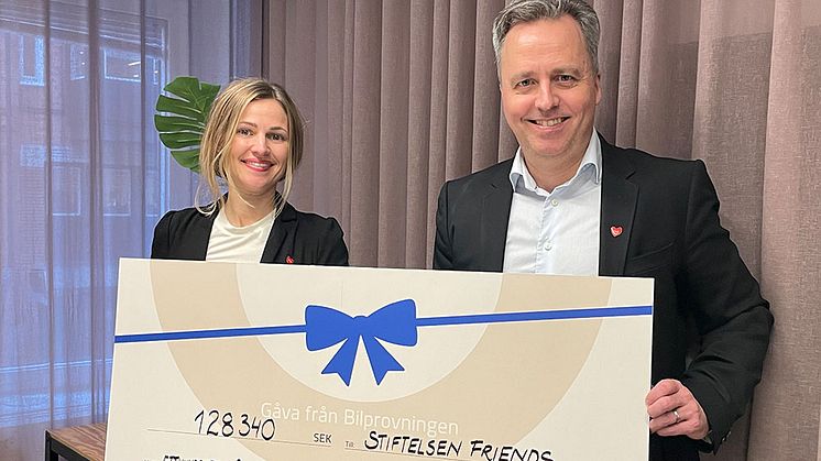 Här tar Friends generalsekreterare Maja Frankel emot en värdecheck av Bilprovningens vd Niklas Stragne. Försäljningen av HEJ-pins på stationerna har bidragit med ytterligare 130 000 kr till Friends viktiga arbete. Foto: Bilprovningen