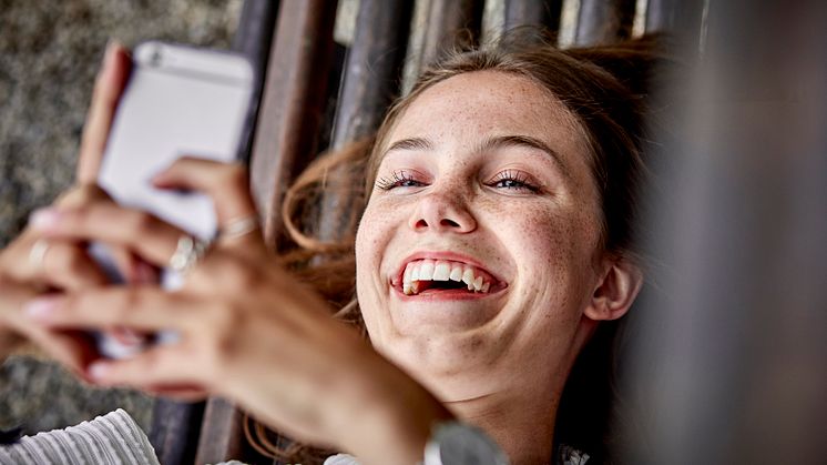 Laughing young woman lying on a bench using cell phone.jpg