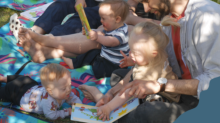 Bild från Svenska Downföreningens småbarnsläger 2023. Tre barn med Downs syndrom tittar i böcker utomhus på en filt.