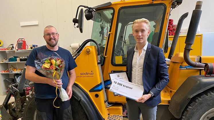 Mattias Askerson (M), ordförande utbildnings- och arbetsmarknadsnämnden överlämnar blommor och prischeck till Henrik Apell, platschef Sodexo Sigtuna. Pressbild: Sigtuna kommun 