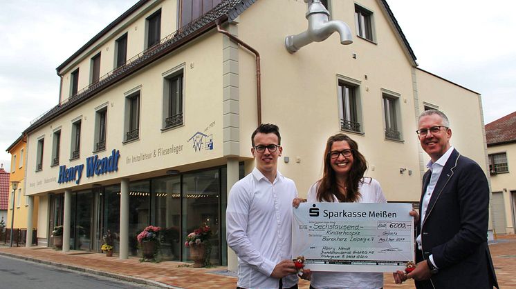 Hendrik Wendt, Ulrike Herkner und Henry Wendt mit dem Spendenscheck für Bärenherz vor dem neuen Geschäftshaus