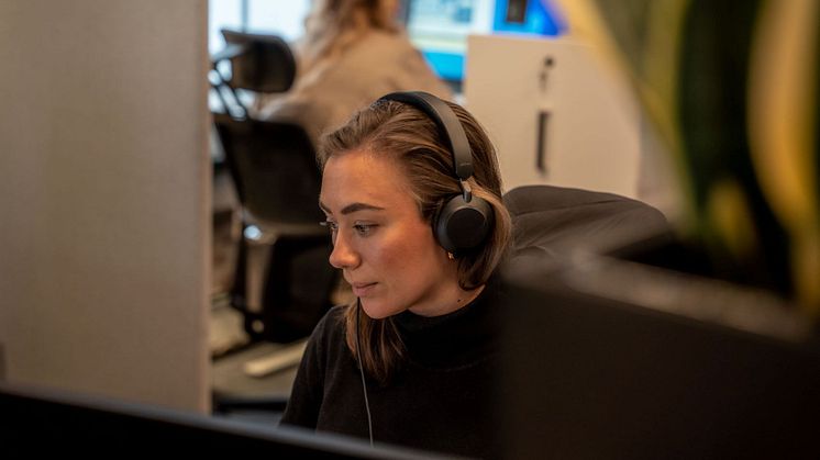 Person sitter ved PC-en med hodetelefoner på, dypt fokusert på oppgaven foran seg.