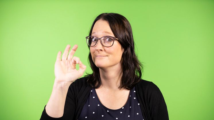 Maria Norberg, konsult på Teckenbro, medverkar i seminariet "Hög tid för teckenspråkiga böcker!" på Bokmässan 2021. På fotot gör hon tecknet perfekt mot en grön bakgrund. Foto: Mikael Sundberg/MTM.