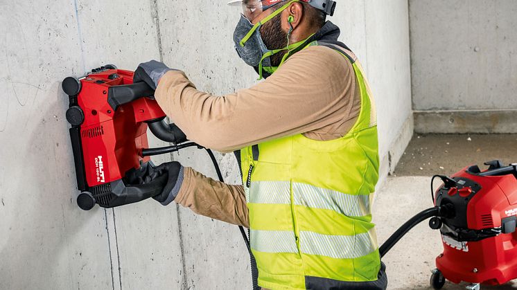 Mann slisser spor i betong til rør eller kabler. Maskin koblet til støvsuger for støvfri slissing.