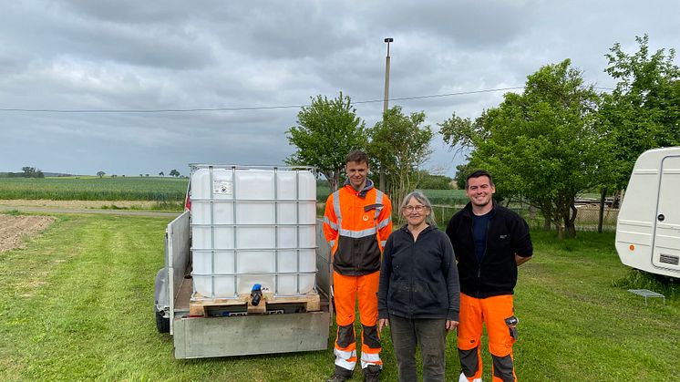 Ursula Rauwolf (mit Sebastian Pfaff, r., und Rico Huhn) von der Baumwege-Initiative Grimma freut sich über die Lieferung des ersten Behältnisses, in dem Regenwasser zum Gießen der Bäume aufgefangen werden soll.