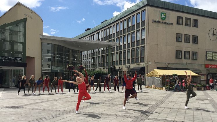 DIS/Dans i Stockholms stad och län erbjuder ungdomar sommarjobb som dansare. Syntolkning: Rödklädda dansare uppträder på ett torg.  