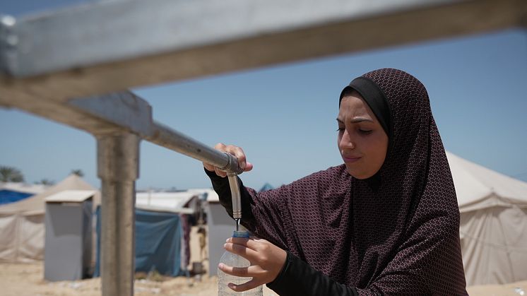 Duaa Abu Sabha fyller på vattenflaskor från Oxfams vattentank, som installerats i Al-Malwasi, Gaza. Foto: Alef Multimedia/Oxfam