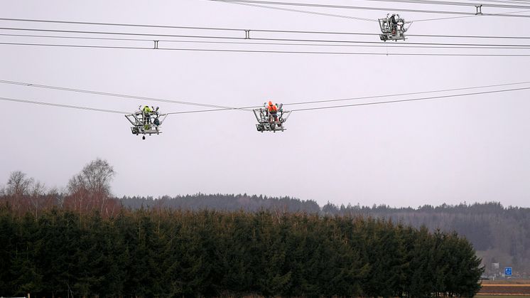 Hochspannungsmonteure arbeiten in speziellen Leitungsfahrwägen um Abstandshalter zwischen den Leiterseilen zu montieren. (Bernd Feil / LEW)