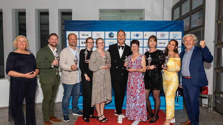 Björn Donner (Mitte mit Fliege) mit den Preisträger*innen des Service Award 2024, gerahmt von Stadtpräsidentin Bettina Aust und Uwe Wanger, Geschäftsführer Kiel-Marketing