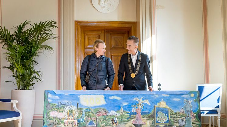 Konstnären Jeremia Håkan Andersson överlämnar en tavla till kommunfullmäktiges ordförande Aslan Akbas. Foto: Kristin Lidell