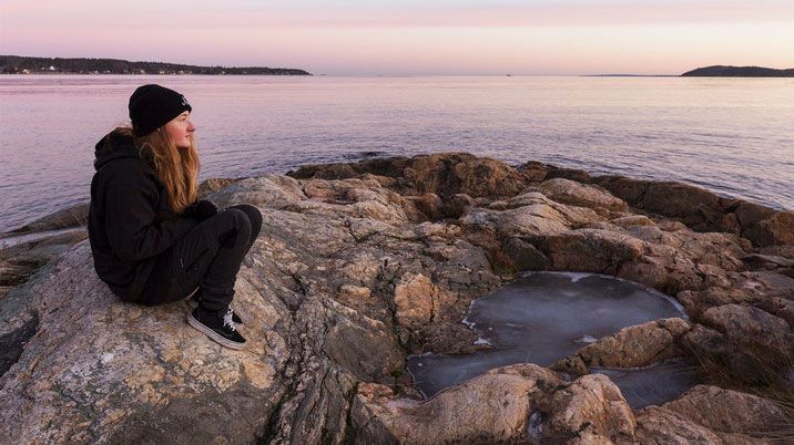Flicka med svart mössa som sitter på en klippa och titta ut över havet. 