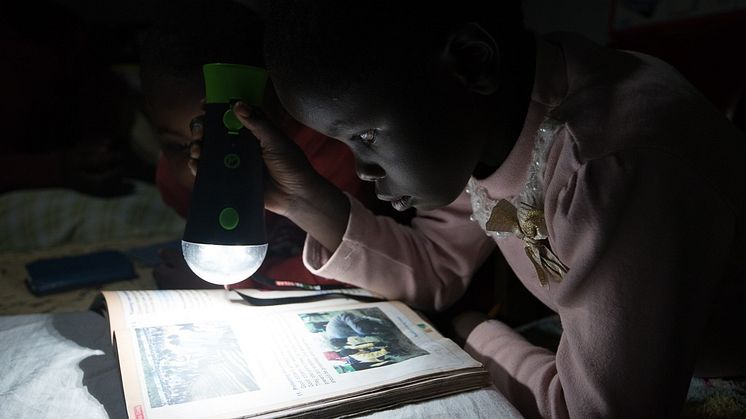 A child in Kenya is reading in the light from off-grid solar energy. SunFunder borrower [M-KOPA], Kenya.