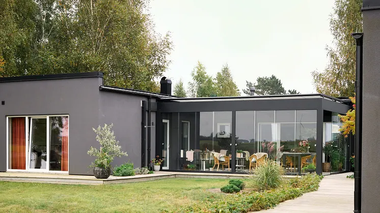 En modern pergola med svarta profiler från Classicum, i anslutning till ett grått hus.