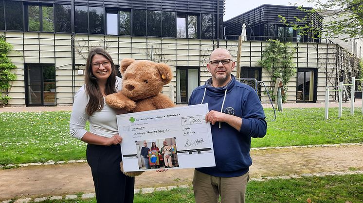 Ulrike Herkner und Stephan Weinholz präsentieren stolz den Spendenscheck vor dem Kinderhospiz Bärenherz