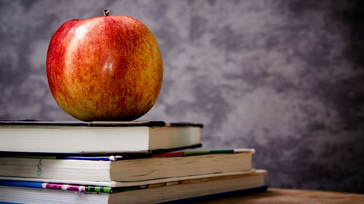 Bilde av ett eple oppå en stabel med bøker. Skolefrukt-ordningen var et lovpålagt tiltak ved alle Norges ungdomsskoler og kombinerte barne- og ungdomsskoler. Illustrasjonsfoto: Stocksnap.io