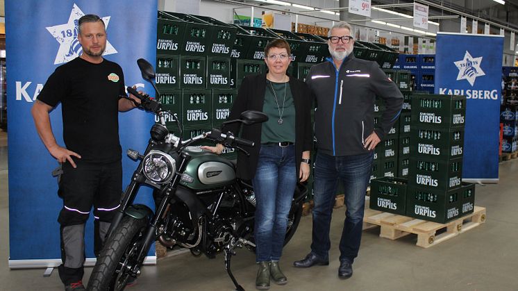 Globus-Mitarbeiter Alex Kunz (links) und Karlsberg-Gebietsverkaufsleiter Axel Piro (rechts) übergaben der glücklichen Gewinnerin Sabrina Kiefer ihre Karlsberg UrPils Ducati Scrambler. Foto: Karlsberg