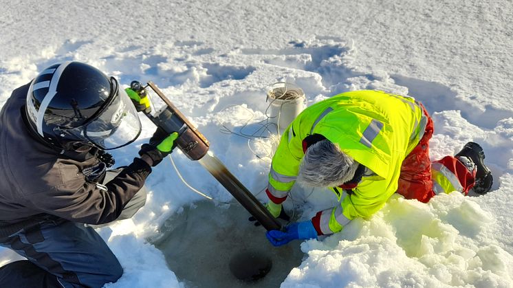 Erling Fjelldal fra NIBIO Svanhovd (med scooterhjelm) og Geir Dahl-Hansen fra Akvaplan-niva tar sedimentprøver i Firkantvann. Foto: Tore Flatlandsmo Berglen, NILU