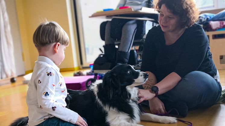 Yvonne Christ und Therapiebegleithündin Tille sitzen bei einem Besuch in der Kindertagesstätte Storchennest gemeinsam mit Ben-Noah zusammen. Im Hintergrund Christs Projektassistentin.