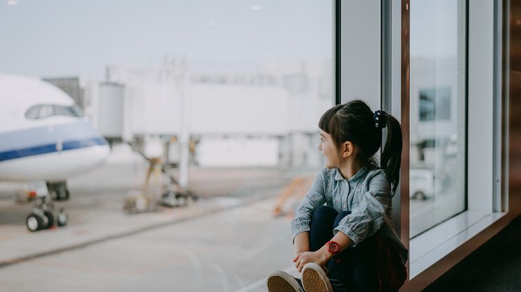 Preschool girl sitting by window at airport and looking outside