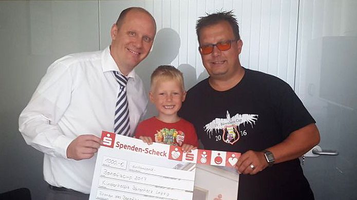 Hendrik Pacyna von der Deutuna Finanzplanung GmbH, der kleine Jona und Jörg Thiele präsentieren stolz den Spendenscheck für das Kinderhospiz Bärenherz
