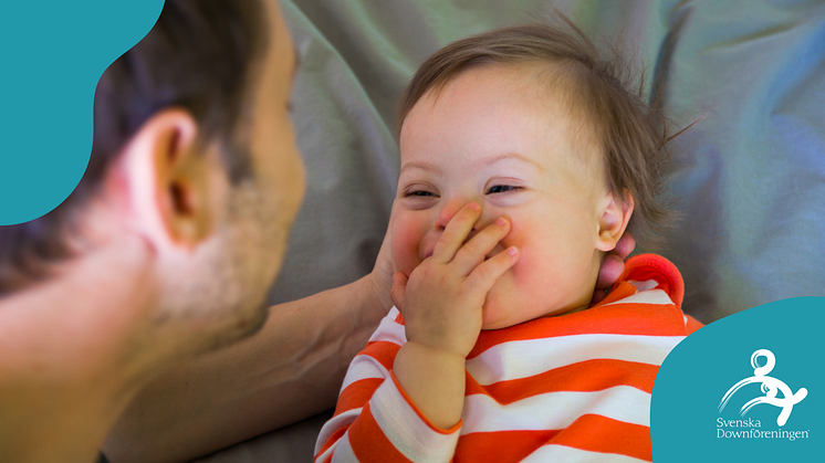 Baby med Downs syndom ler mot vuxen person