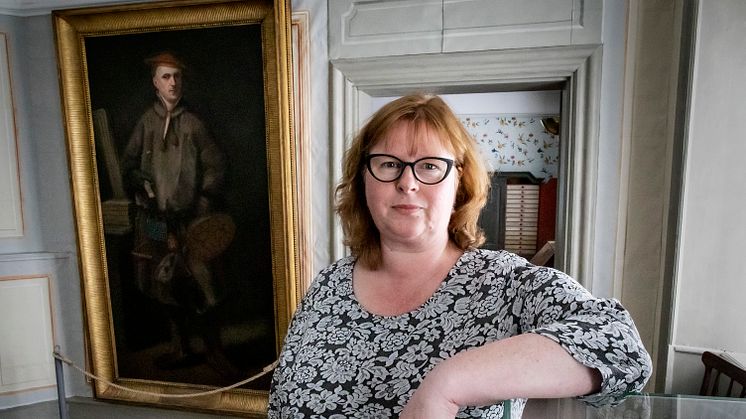 Annika Windahl Pontén standing in front of a portrait of Carl Linnaeus.