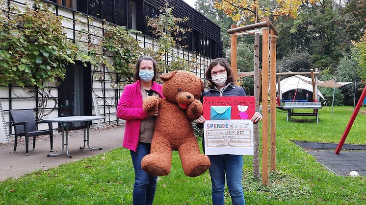 Kerstin Stadler (li.) und der Bärenherz-Bär (Mitte) nehmen den Scheck von Aline Engelmann entgegen