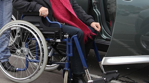 Resenär som får hjälp från rullstol till bil.