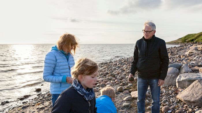 Familj på fyra personer som har en avslappnande stund vid havet och letar stenar och snäckor.