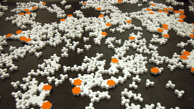 Del av stort experiment med 100 aktiva robotar. Robotar syns i orange och passiva byggnadsblock är vita. 