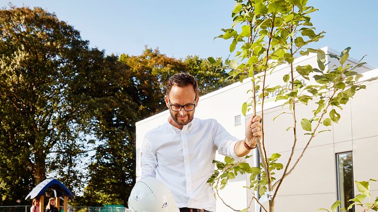 Marko Drazovic planterade ett äppelträd under invigningen av förskolan Utforskaren i Helsingborg. Christian Ahlkrona, projektchef på Midroc, assisterade. 