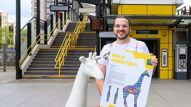 Artist, Aaron Bevan, poses outside of East Croydon station with one of the giraffe sculptures 