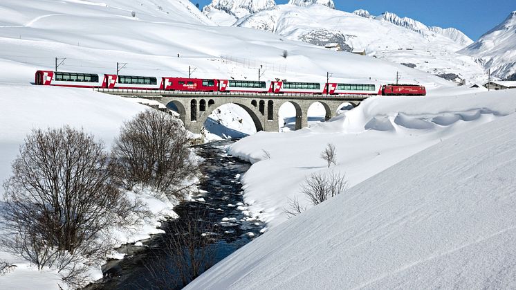 Der Glacier Express überquert im zugeschneiten Urserental in der Nähe des Dorfes Hospental im Kanton Uri die Furkareuss 