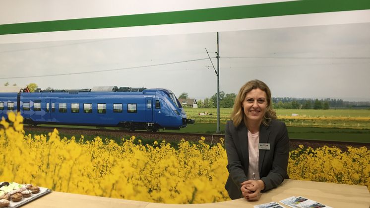 Maria Parent framför en bild på ett Pågatåg i Skåne. Ett exempel där Alstom har levererat regionaltåg till Sverige.