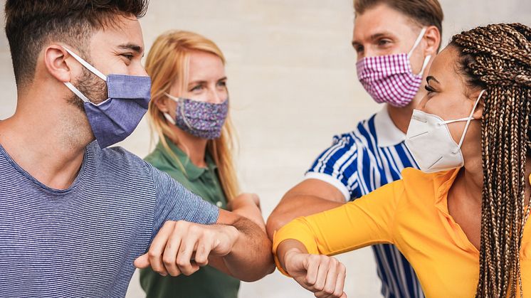 Vier Studierende tragen Masken und begrüßen sich mit dem Ellenbogen.