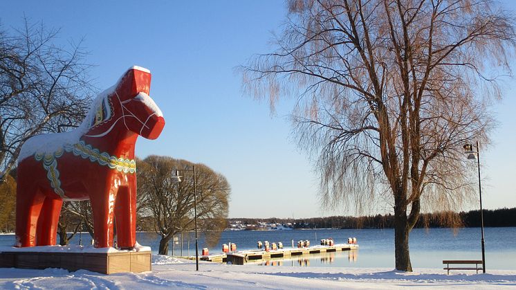 Syntolkning: Röd dalahäst i vinterlandskap. 