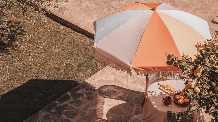 Loulé är ett blockrandigt parasoll i rosa, vitt, korall och orange med naturfärgade bomullsfransar.