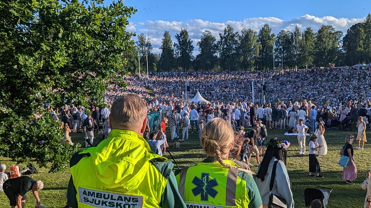 Två ambulanssjuksköterskor, Mattias Andersson och Terese Jonsson, står med ryggen mot kameran och ser ut över en stor folksamling.