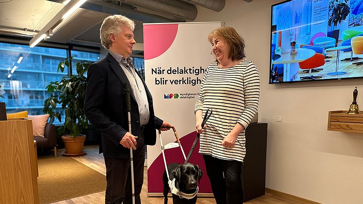 Bildtext: SRF:s förbundsordförande Niklas Mattsson räcker symboliskt över en ledarhund i sele till MFD:s generaldirektör Malin Ekman Aldén. ﻿Foto: Monica Walldén. 