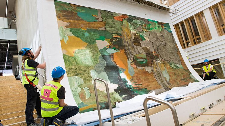 Andreas Erikssons målning "Stenbrottet" installeras i den nya huvudentrén. Foto Anna Molander. Syntolkning: Tre personer i skyddskläder monterar en stor abstrakt väggmålning.