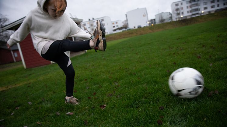 Familjehem - pojke som sparkar på en fotboll. Han är på en gräsplan.