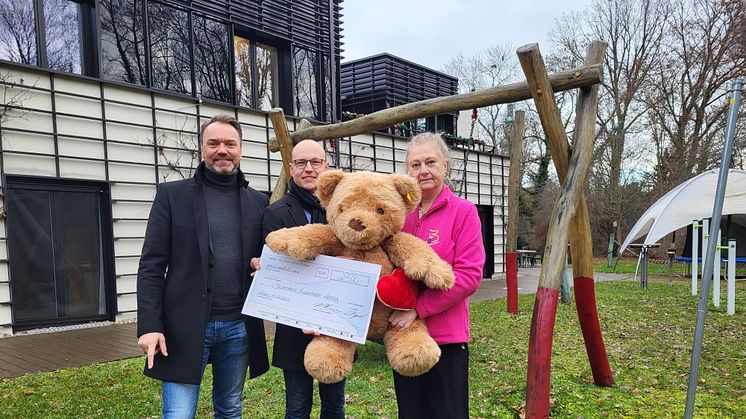 Die Geschäftsführer der Physio Holding GmbH, Holger Hermann und Bastian Vogel, präsentieren mit Elvira Wegner vom Kinderhospiz stolz den Spendenscheck im Bärenherz-Garten