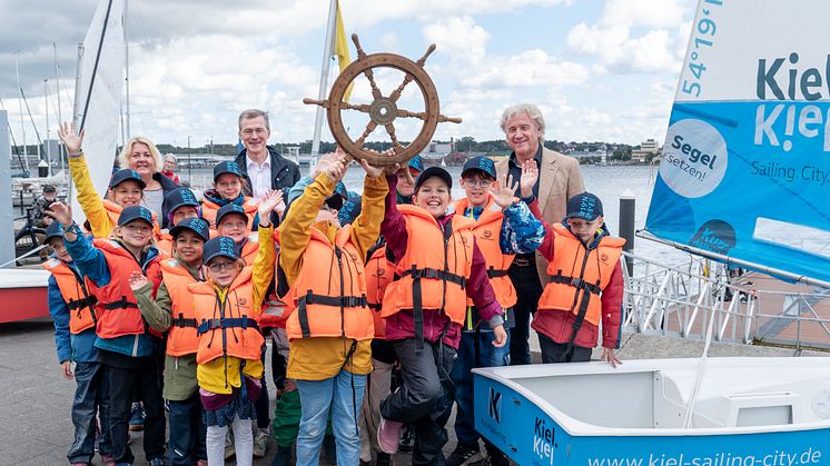 Bettina Aust (Stadtpräsidentin), Frank Meier (Stadtwerke Kiel) und Uwe Wanger (Kiel-Marketing) erhalten zum Saisonende das Steuerrad zurück von den Schüler*innen der Friedrich-Junge-Grundschule