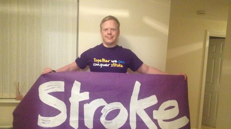 Richard Gillard in a Stroke Association purple top, holding a purple Stroke Association flag. 