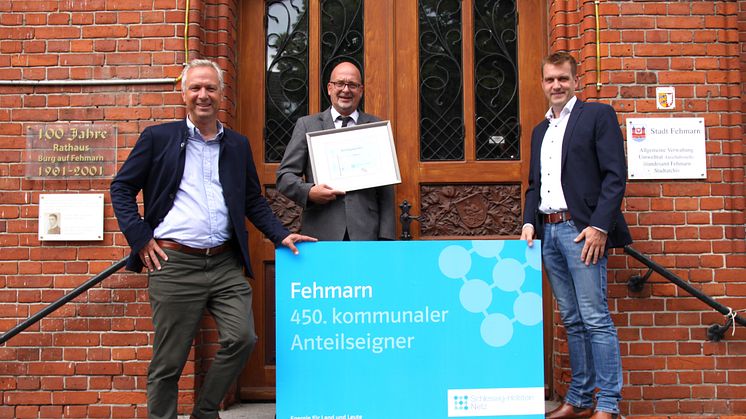 Foto: SH Netz - Symbolische Aktienübergabe vor dem Rathaus (v.l.) Matthias Boxberger, Aufsichtsratsvorsitzender bei SH Netz, Bürgermeister Jörg Weber und Mirko Sadowski, Leiter des Technik-Standortes von SH Netz im Kreis Ostholstein.