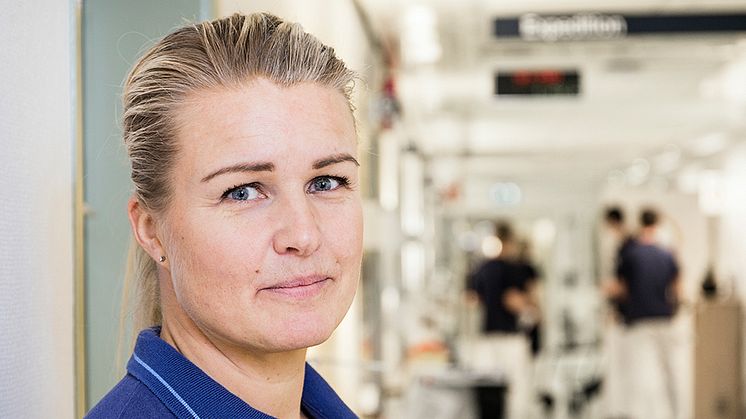 Mari Andersson har sett hur viktig konsten kan vara för patienterna och deras anhöriga. Foto: Anna Molander. Syntolning: Mari i arbetskläder i korridoren på geriatriken.