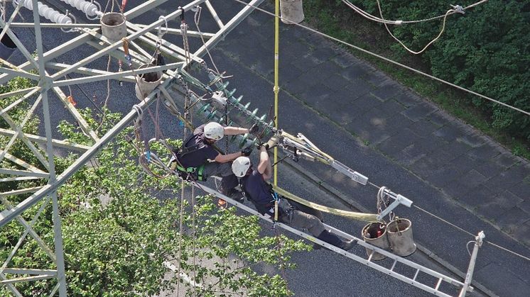 Aus der Drohnenperspektive: Maximilian Selge (links) und Carsten Hartwich lösen die alte 110.000 Volt-Abspannkette, nachdem sie diese zuvor mit Hilfe eines Kettenzuges entlastet haben. Foto: SH Netz